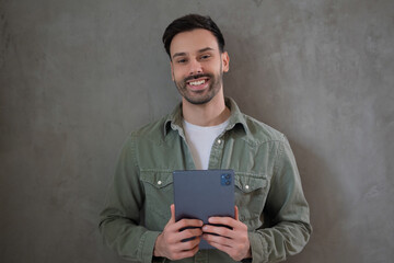 Smiling man holding a tablet against gray wall