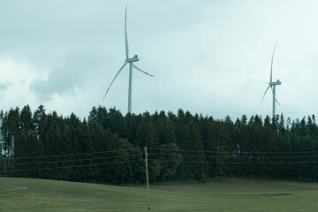 Wind turbines tower over a vast green field near a forest on an overcast day in the countryside