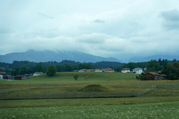 Rolling green hills and houses under a cloudy sky in a serene countryside landscape near the mountains