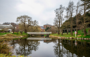 Obraz premium Tranquil Park Landscape Featuring a Wooden Bridge and Calm Reflective Pond in Botanical Garden, Copenhagen, Denmark, 16 April 2018