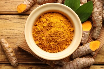 Turmeric powder in bowl, roots and leaves on wooden table, flat lay