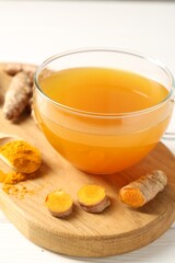 Aromatic turmeric tea in glass cup, roots and powder on white table, closeup