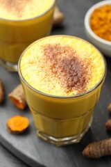 Delicious turmeric latte, powder and rhizomes on black wooden table, closeup