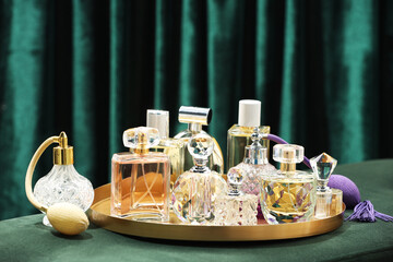 Different luxury perfumes on green pouf near teal curtains