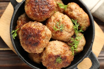 Tasty patties and dill in frying pan on wooden table, top view