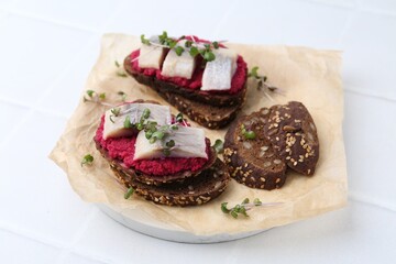 Tasty sandwiches with herring and horseradish sauce on white tiled table, closeup