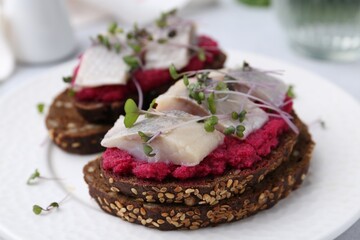 Tasty sandwiches with herring and horseradish sauce on plate, closeup