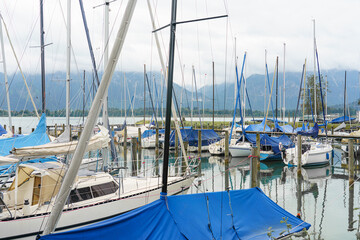 Sailboats anchored at a marina under cloudy skies with mountains in the background near a waterway