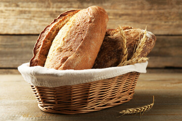 Different loaves of fresh bread and spikes in wicker basket on wooden table, closeup
