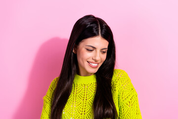 Portrait of a cheerful young woman wearing a vibrant green sweater against a pink background