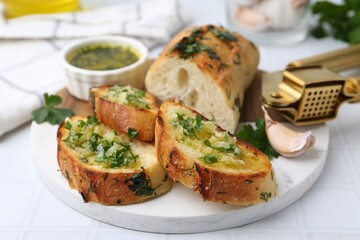 Tasty bread with garlic, herbs and oil on white tiled table, closeup