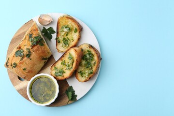 Tasty bread with garlic, herbs and oil on light blue background, top view. Space for text