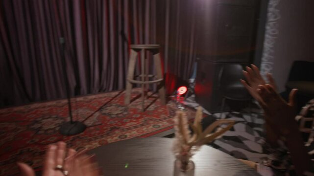 POV view of woman siting at table with her African American friend, watching stand-up performance together
