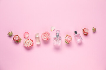 Bottles of perfume and beautiful flowers on pink background, flat lay