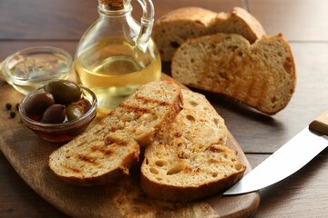 Toasted bread with oil, olives and spices on wooden table, closeup