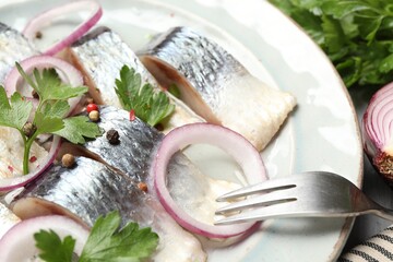 Pieces of delicious herring with spices and onions served on table, closeup