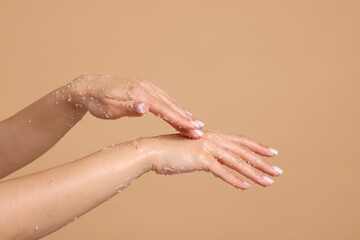 Naklejka premium Woman applying body scrub onto her hands on beige background, closeup