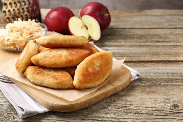 Delicious fried pyrizhky (stuffed pies) and apples on wooden table, closeup. Space for text