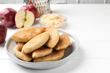 Delicious fried pyrizhky (stuffed pies) and apples on white wooden table, closeup. Space for text