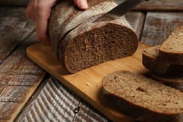 Woman cutting fresh bread at wooden table, closeup