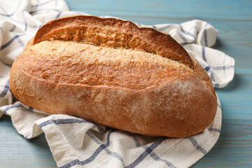 Fresh loaf of bread on light blue wooden table, closeup
