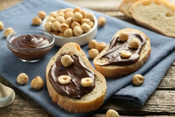 Slices of bread with chocolate spread and hazelnuts on wooden table, closeup