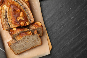 Cut banana bread with nuts on black table, top view. Space for text