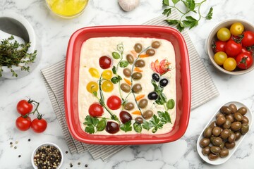 Raw focaccia with vegetables, olives and spices on white marble table, flat lay