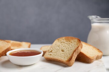 Slices of tasty toasted bread, milk and jam on white table against grey background, closeup