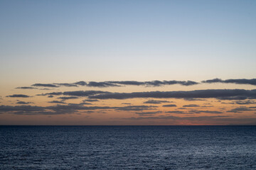 The sky is a beautiful shade of blue with a few clouds scattered throughout. The ocean is calm and peaceful, with no signs of any activity. The scene is serene and tranquil