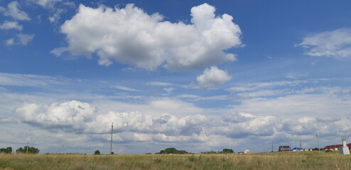 Fluffy clouds drift across a bright blue sky over open fields in the countryside during...