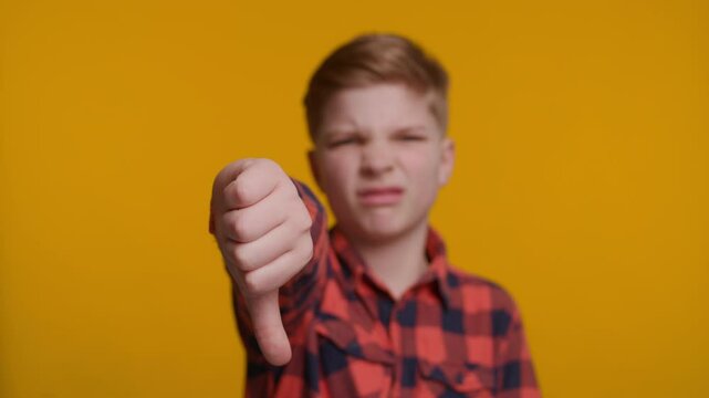 Boy Showing Thumbs Down at Camera on Yellow Background
