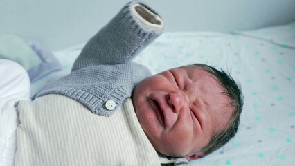 Close-up of a newborn baby crying with eyes tightly shut and face scrunched, capturing the raw...