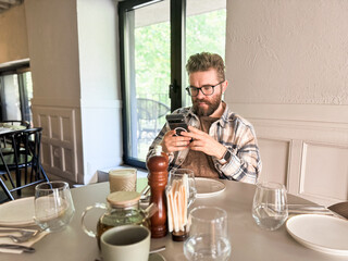Man browsing phone at cafe table. Modern lifestyle, digital habits and casual urban dining