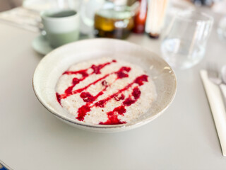 Oatmeal with berry drizzle on restaurant table. Healthy eating, minimalist style and natural breakfast choices