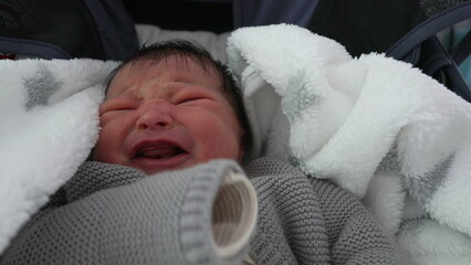 Newborn baby bundled in a cozy blanket, crying and showing signs of distress, capturing an...