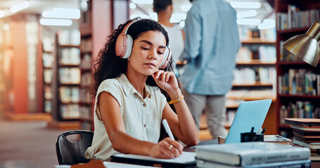 Student, headphones and writing in library for university, woman and studying for education or project. Female person, notes and academy campus with literature, research and assignment for knowledge