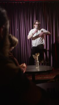 Vertical over the shoulder shot of male stand-up artist telling joke from stage and audience clapping