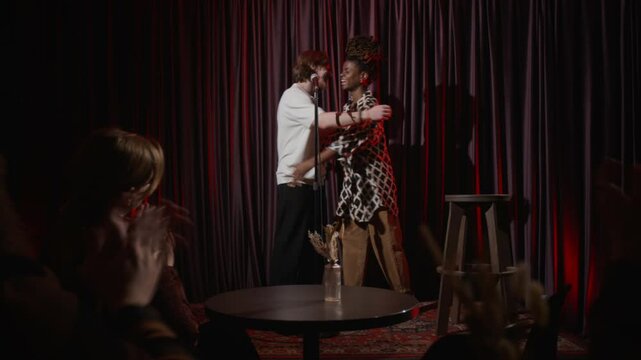Young male stand-up artist inviting his colleague on stage and hugging her before continuing performance together