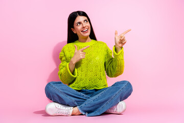 Young woman in casual style seated against a pink background, expressing positivity through...