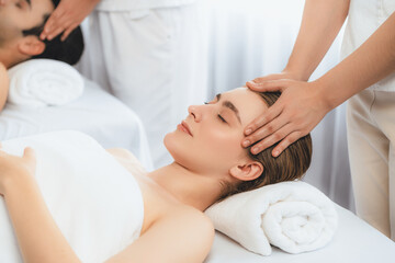 Caucasian couple enjoying relaxing anti-stress head massage and pampering facial beauty skin recreation leisure in dayspa modern light ambient at luxury resort or hotel spa salon. Quiescent