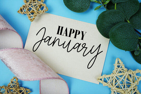 Happy January text on paper card with fabric ribbon and rattan star decorations on blue background - Powered by Adobe