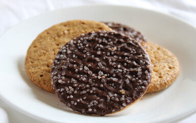 Close-up of digestive biscuits isolated on a white plate. two are plain and the other are coated in dark chocolate and sprinkled with sugar crystals.