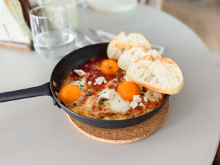 Shakshuka served hot in pan with bread slices. Comfort food, modern brunch and urban culinary style