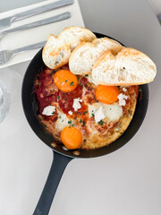Shakshuka served hot in pan with bread slices. Comfort food, modern brunch and urban culinary style