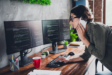 Young female programmer working on code at a dual monitor setup in a stylish office workspace while multitasking