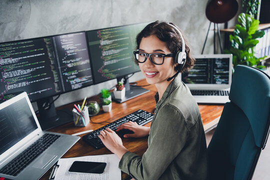 Young female software developer working remotely on a programming project, smiling confidently in a modern home office environment