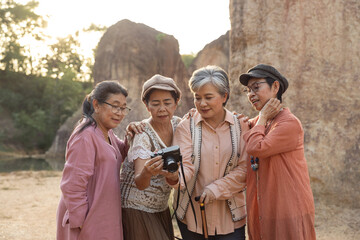 Asian senior women friends gathering closely together smiling looking at camera screen reviewing photo results during outdoor trip sharing joyful moment with warm connection and happiness.