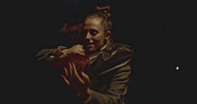Two friends meet in a park at night, greet each other with a hug, and wave goodbye as one leaves.