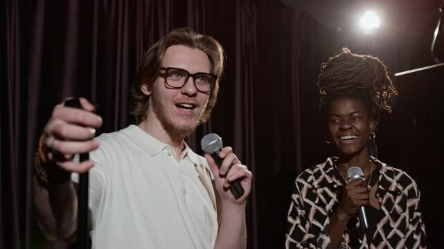 Man, holding microphone, having conversation with African American woman on stage during their stand-up performance